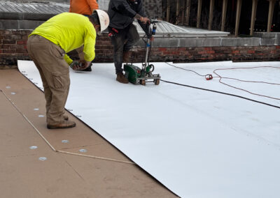 Three men are collaborating on a roof, handling a large white sheet as part of their work.