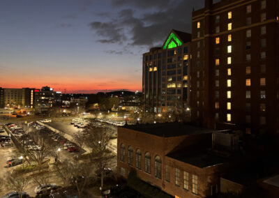 A panoramic view of the city skyline at dusk, illuminated by city lights, as seen from a hotel balcony.