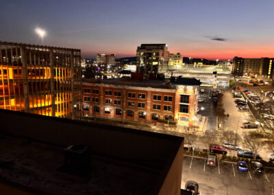 A panoramic view of the city skyline at dusk, illuminated by city lights, as seen from a hotel balcony.